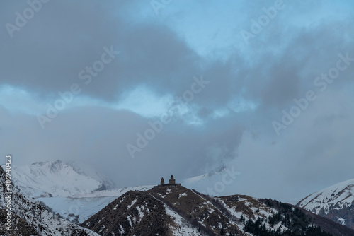 Old Georgian church in the high snow covered mountains and clouds. Winter landscape. Kazbegi Georgia.
