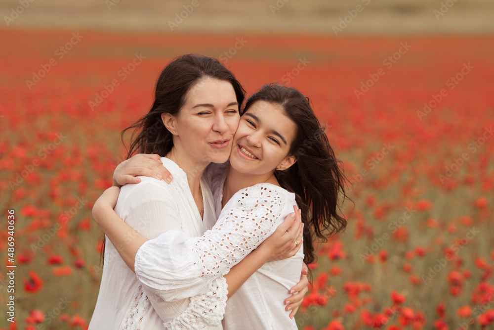 Naklejka premium Beautiful mom and teen daughter in white dresses on a poppy field