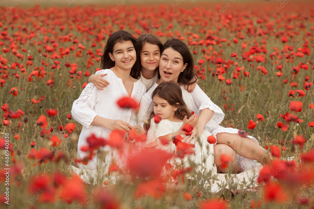 Portrait of a large family in a poppy field. Happy mom and daughters in white dresses hugging and laughing Portrait of a large family in a poppy field. Happy mom and daughters in white dresses hugging and laughing