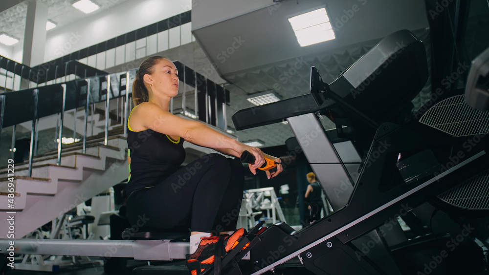 Fit Athletic Baby Woman Work out on Rowing Machine, Doing Her Fitness Exercise. Girl Activity Training in Modern Gym. Sports Female Workout in Exercising on Row Machine Fitness Center. Fit Athletic Baby Woman Work out on Rowing Machine, Doing Her Fitness Exercise. Girl Activity Training in Modern Gym. Sports Female Workout in Exercising on Row Machine Fitness Center.