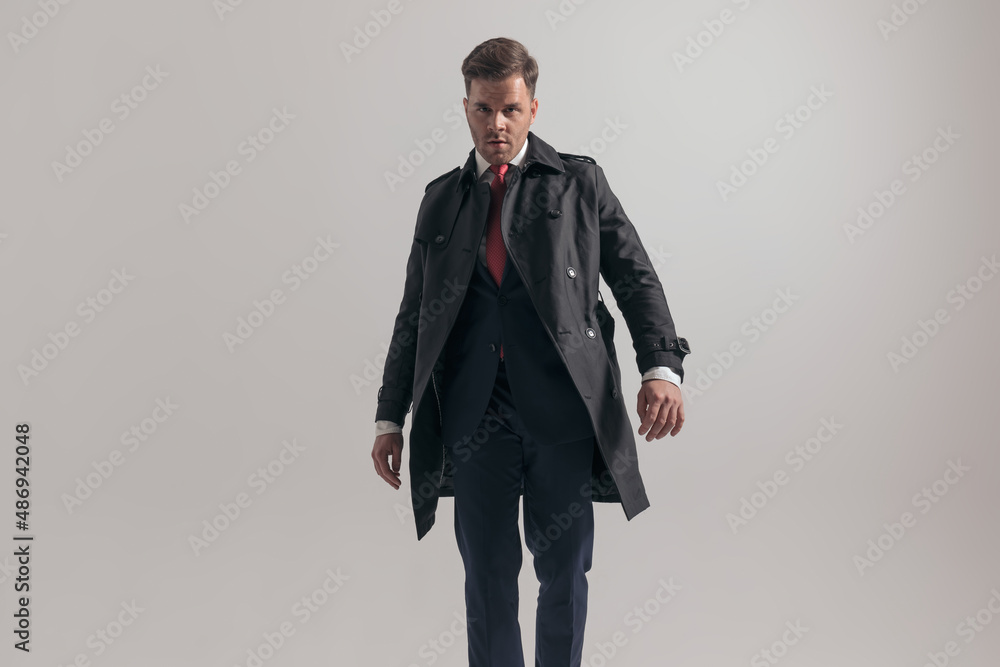 handsome businessman in suit with long coat posing on grey background handsome businessman in suit with long coat posing on grey background
