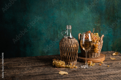 A glass of homemade white wine with grapes and a bottle on a rustic wooden table