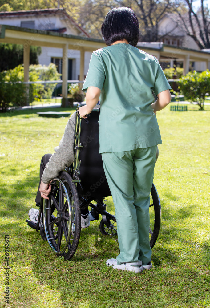 Obraz premium Caucasian senior on the wheelchair helped by nurse outdoor. Retired elderly people living their life at its best.