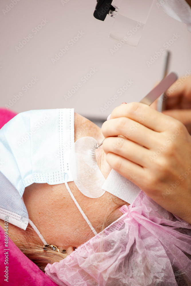 Fototapeta premium A girl makes the procedure for extending eyelashes during a pandemic, a master with tools in her hands