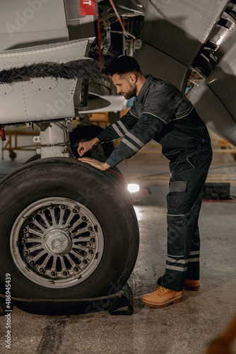 Full length of bearded man aviation maintenance technician repairing aircraft landing gear at repair station