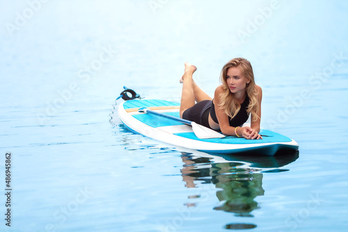 The girl is resting and sunbathing on a surfboard. Young athletic woman posing while lying on a surfboard. © Svetlana