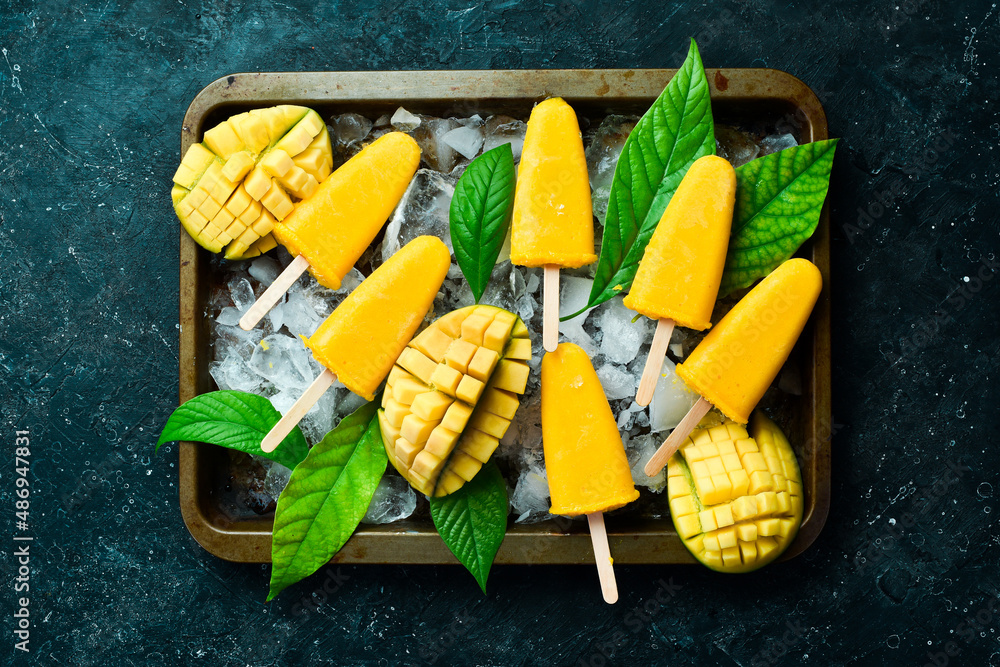 Frozen mango popsicles on a tray. Cold summer sweets. On a black stone background. Top view. Frozen mango popsicles on a tray. Cold summer sweets. On a black stone background. Top view.