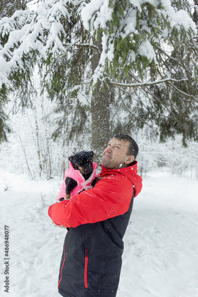 A man holds a small dog in his arms in a public park in winter. Positive emotions. Pets