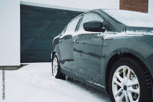 a gray car is covered with snow against the background of a garage of a private house