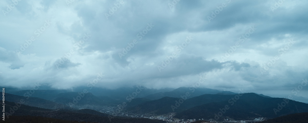Moody rain clouds above mountains. Panoramic view of dark sky in mountainside