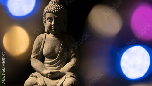 Close-up on the statue of the Buddha of Serenity, on a black background surrounded by luminous circles