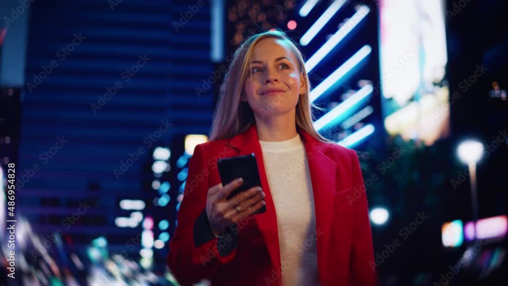Portrait of a Beautiful Woman in Red Coat Walking in a Modern City Street with Neon Lights at Night. Attractive Female Using Smartphone and Looking Around the Urban Cinematic Environment. Portrait of a Beautiful Woman in Red Coat Walking in a Modern City Street with Neon Lights at Night. Attractive Female Using Smartphone and Looking Around the Urban Cinematic Environment.