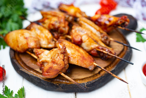 A hearty snack for the family: Delicious grilled chicken wings on skewers on a beautiful board on a white background. Close-up