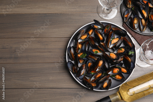 Cooked mussels with parsley and white wine served on wooden table, flat lay. Space for text
