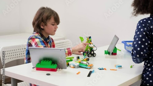 Students In School Computer Coding Class Building And Learning To Program Robot Vehicle. Multi ethnic children making science, technology and coding tasks at school with tablet. Modern education