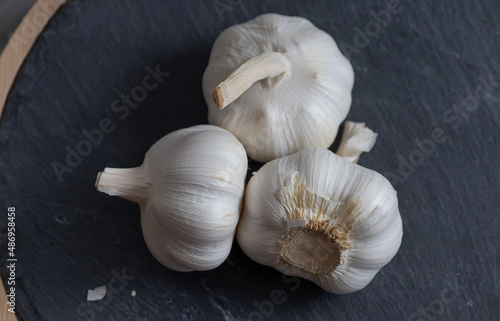 Three bulbs of garlic lie on a stone cutting board. Close-up. View from above.