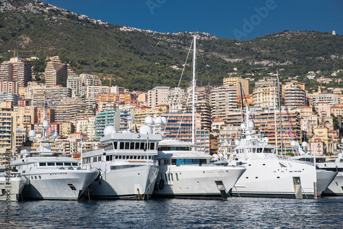 A lot of huge yachts are in port of Monaco at sunny day, megayachts are moored in marina, is a yacht show, Monte Carlo, real estate housing is on background, glossy board of the motor boat © Vladimir Drozdin