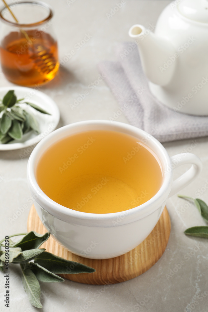 Cup of aromatic sage tea and fresh leaves on light grey table Cup of aromatic sage tea and fresh leaves on light grey table