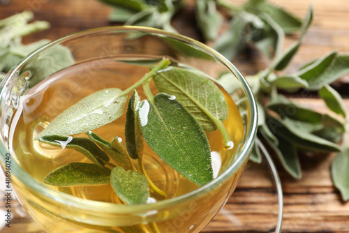 Foto Cup of aromatic sage tea with fresh leaves on wooden table, closeup