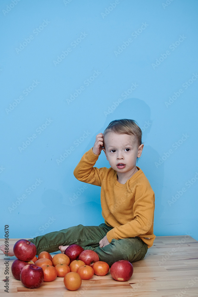 a boy of 2 years sits on a wooden table and plays with apples and tangerines, he closes his eyes and plays a game.
