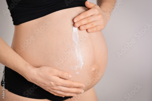 Pregnant woman skin care moisturizer cream on belly. Pregnant woman applying cream at her belly for prevention of stretch marks on the skin in light room.