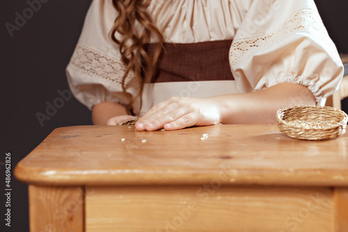 The hands of a girl in a national ethnic folk costume are sorting rice grains. Rice is scattered on a wooden table, close-up