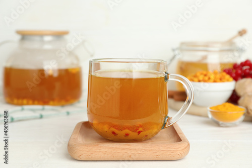 Glass cup of immunity boosting tea with ingredients on white wooden table