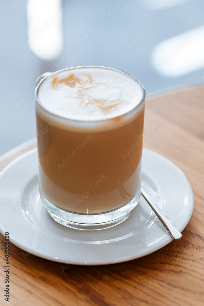 Caffe latte in transparent mug with other mug in first plan, blurred. Barista coffee for international barista day. Break and pause to chill. Coffee with milk and foam. Caffe latte in transparent mug with other mug in first plan, blurred. Barista coffee for international barista day. Break and pause to chill. Coffee with milk and foam.