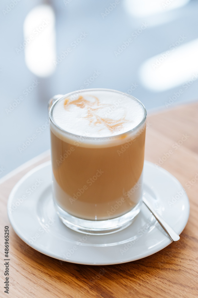 Caffe latte in transparent mug with other mug in first plan, blurred. Barista coffee for international barista day. Break and pause to chill. Coffee with milk and foam. Caffe latte in transparent mug with other mug in first plan, blurred. Barista coffee for international barista day. Break and pause to chill. Coffee with milk and foam.