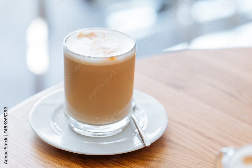 Caffe latte in transparent mug with other mug in first plan, blurred. Barista coffee for international barista day. Break and pause to chill. Coffee with milk and foam. 