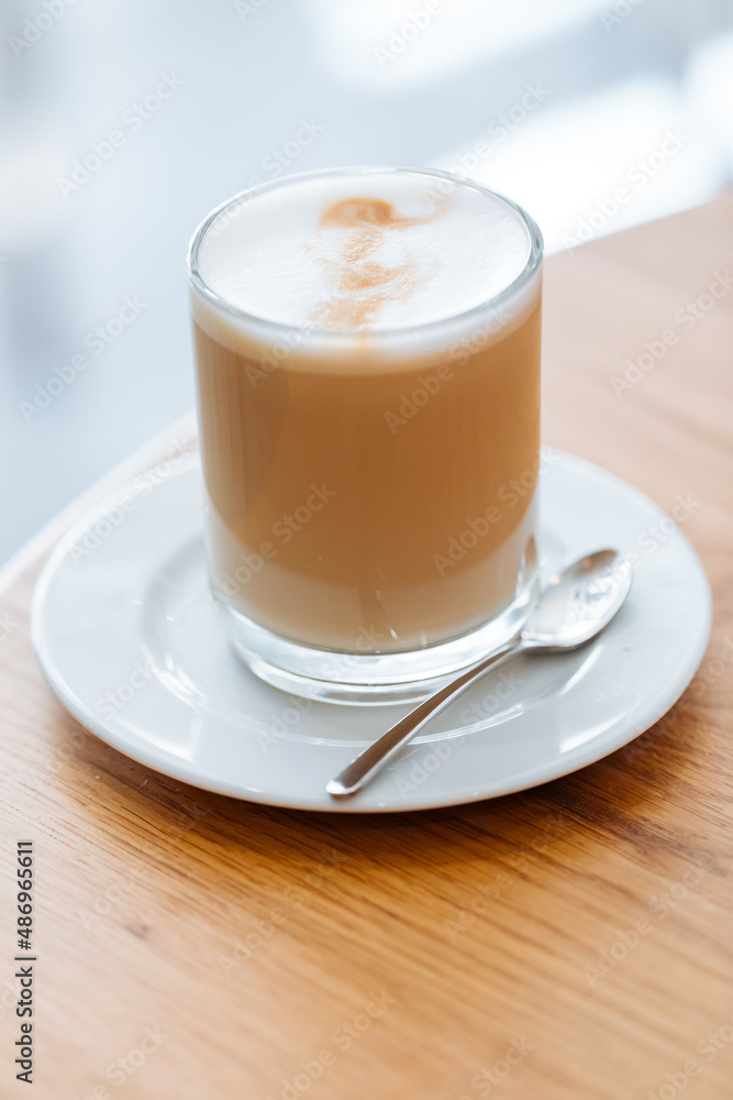 Caffe latte in transparent mug with other mug in first plan, blurred. Barista coffee for international barista day. Break and pause to chill. Coffee with milk and foam. Caffe latte in transparent mug with other mug in first plan, blurred. Barista coffee for international barista day. Break and pause to chill. Coffee with milk and foam.