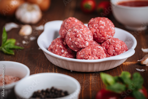 Meatballs in tomato sauce with basil on top. Bright background with ingredients in blurry background. This meal is called Kofte in Turkey and Cufte in Balkans. International meatball day.