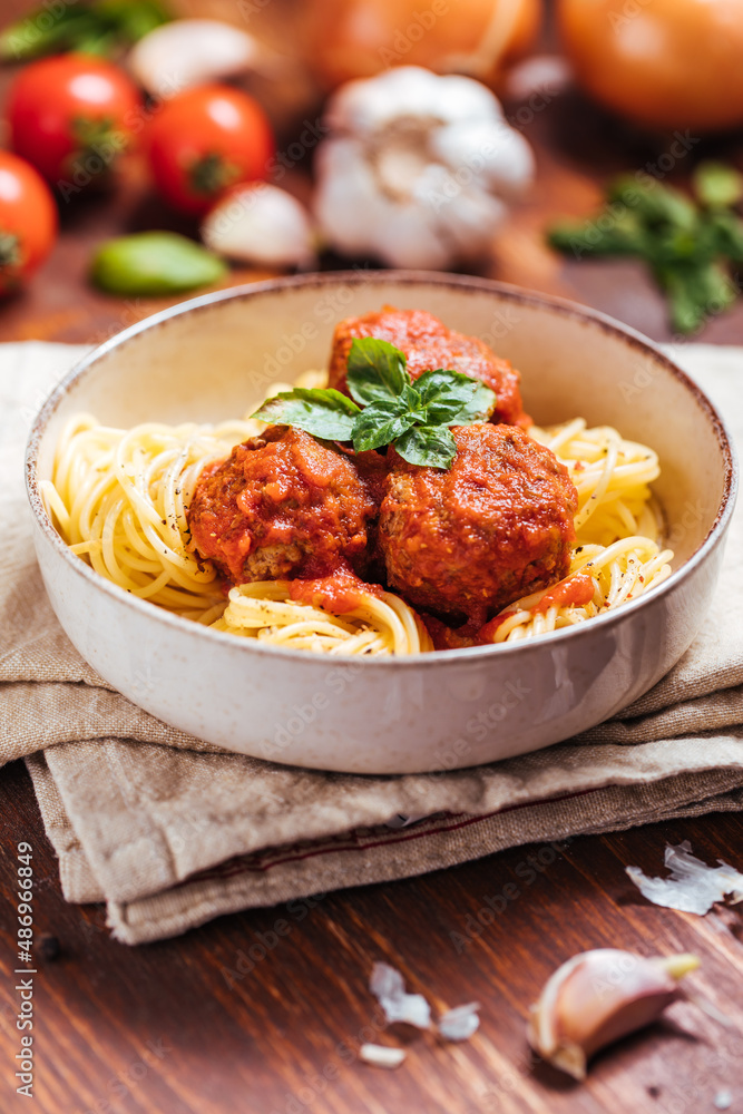 Meatballs in tomato sauce with basil on top. Bright background with ingredients in blurry background. This meal is called Kofte in Turkey and Cufte in Balkans. International meatball day. Meatballs in tomato sauce with basil on top. Bright background with ingredients in blurry background. This meal is called Kofte in Turkey and Cufte in Balkans. International meatball day.