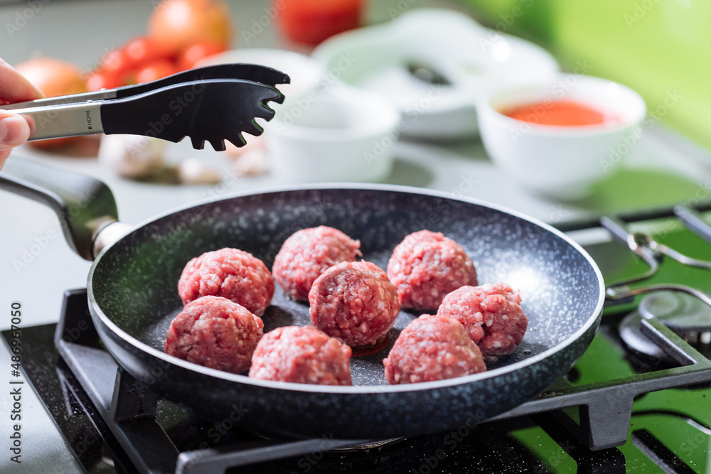Meatballs in tomato sauce with basil on top. Bright background with ingredients in blurry background. This meal is called Kofte in Turkey and Cufte in Balkans. International meatball day. Meatballs in tomato sauce with basil on top. Bright background with ingredients in blurry background. This meal is called Kofte in Turkey and Cufte in Balkans. International meatball day.