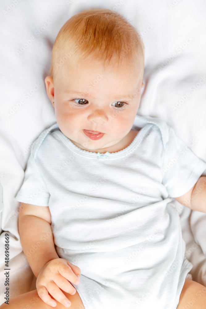 Cute little newborn girl with smiling face looking at camera on white background. Infant baby resting playing lying down on crib bed at home. Motherhood happy child concept Cute little newborn girl with smiling face looking at camera on white background. Infant baby resting playing lying down on crib bed at home. Motherhood happy child concept