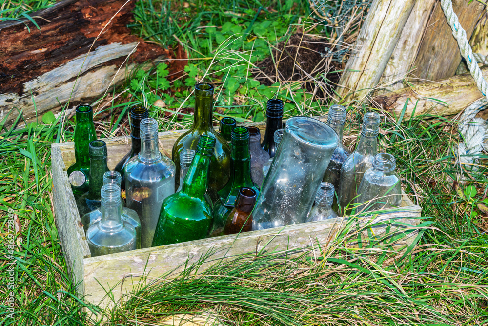 Fototapeta premium Forgotten empty bottles in a wooden box in the grass