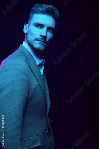 Young handsome model posing in a studio in a trendy neon light. Fashionable man in a stylish suit. Vibrant color. Bright colorful light effects. Disco style. Overlay. Gel filter. Supersaturated