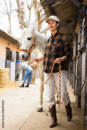 Asian woman horse holder leading white horse on farm. © JackF