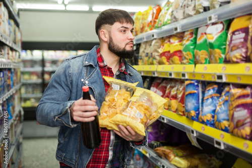 Young bearded man making purchases in shop, choosing snacks for beer photo