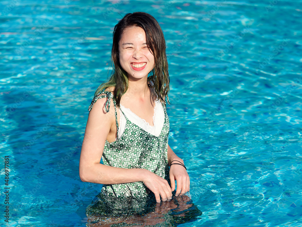Portrait of young Asian woman standing in swimming pool and playing water, beautiful Chinese girl with green hairs in green dress enjoy sunny summer day in water.
