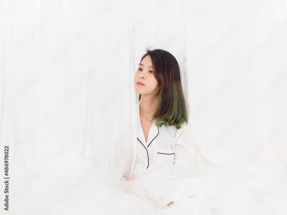 Portrait of young Asian woman sitting and smiling on bed isolated on white curtain background, beautiful Chinese girl with green hairs in white shirt. Portrait of young Asian woman sitting and smiling on bed isolated on white curtain background, beautiful Chinese girl with green hairs in white shirt.