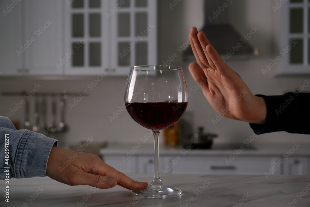 Man refusing to drink red wine in kitchen, closeup. Alcohol addiction treatment