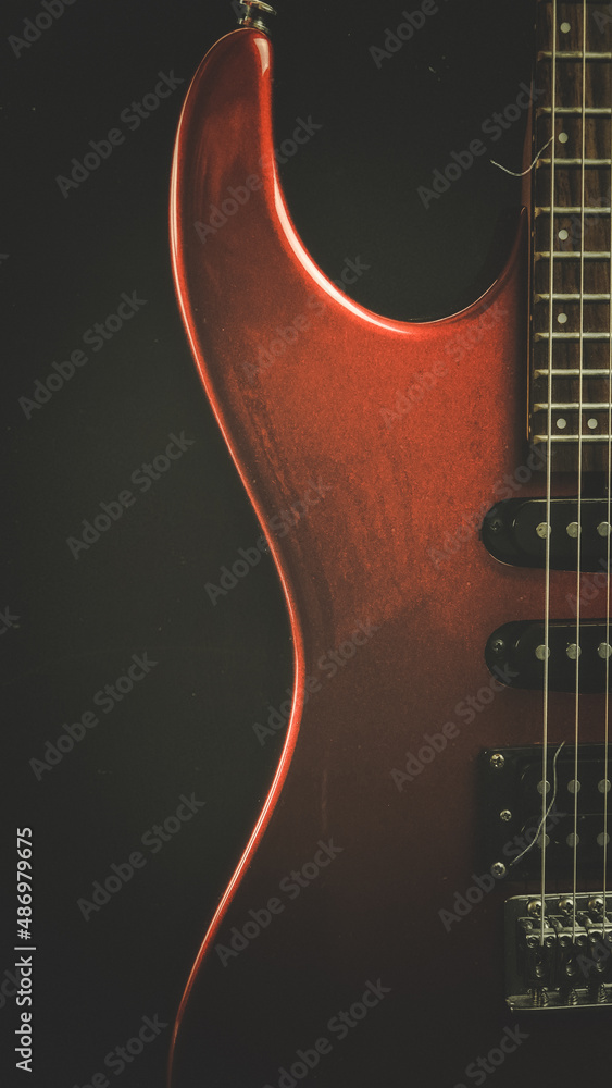 Fototapeta premium A vintage red electric guitar standing upright with textured noir concept as wallpaper. Music concept