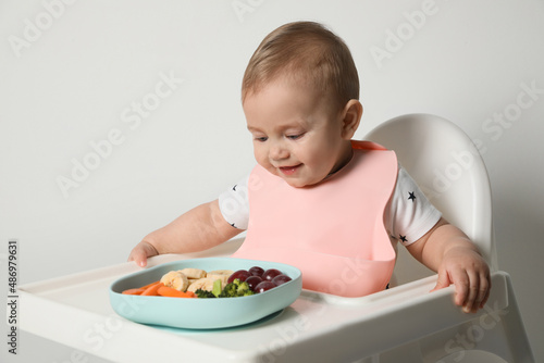 Cute little baby wearing bib while eating on white background