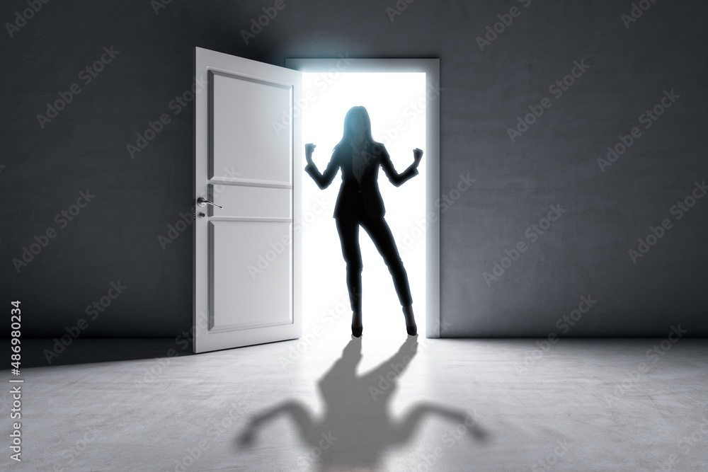 Successful businesswoman standing in front of bright success door in concrete interior with shadow on floor. Future and dream concept. Successful businesswoman standing in front of bright success door in concrete interior with shadow on floor. Future and dream concept.