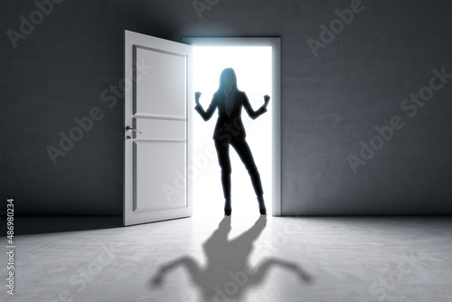 Successful businesswoman standing in front of bright success door in concrete interior with shadow on floor. Future and dream concept.