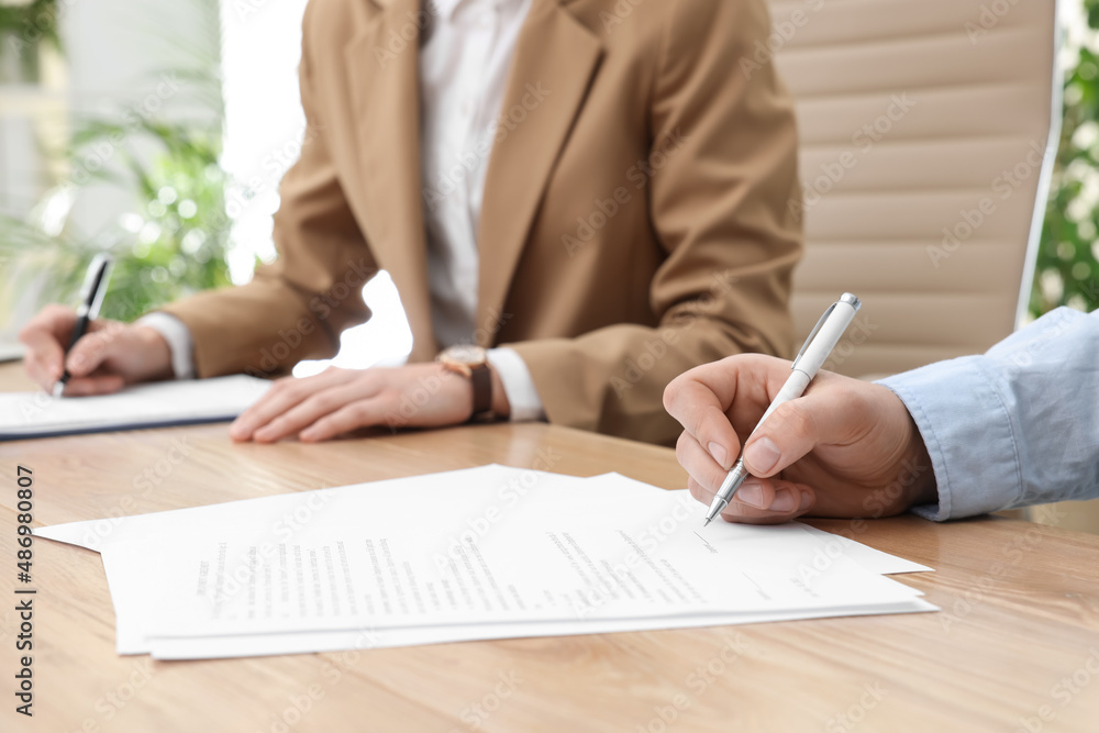 Man signing contract at table in office, closeup. Man signing contract at table in office, closeup.