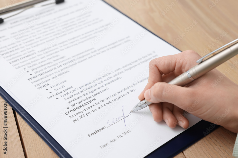 Woman signing contract at wooden table, closeup. Woman signing contract at wooden table, closeup.