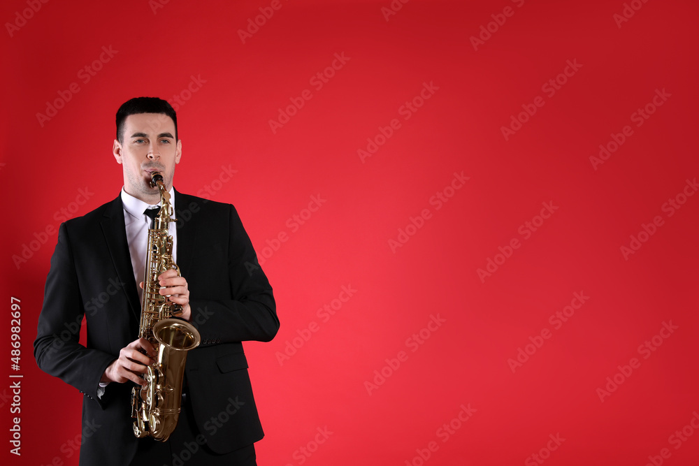 Naklejka premium Young man in elegant suit playing saxophone on red background. Space for text