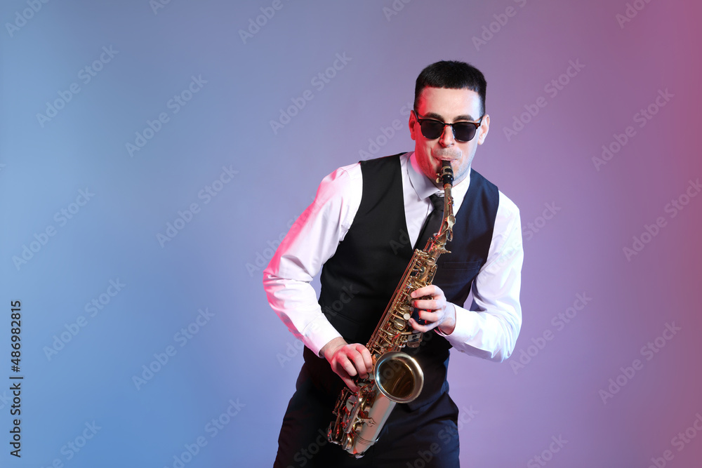 Naklejka premium Young man in elegant outfit playing saxophone on color background. Space for text